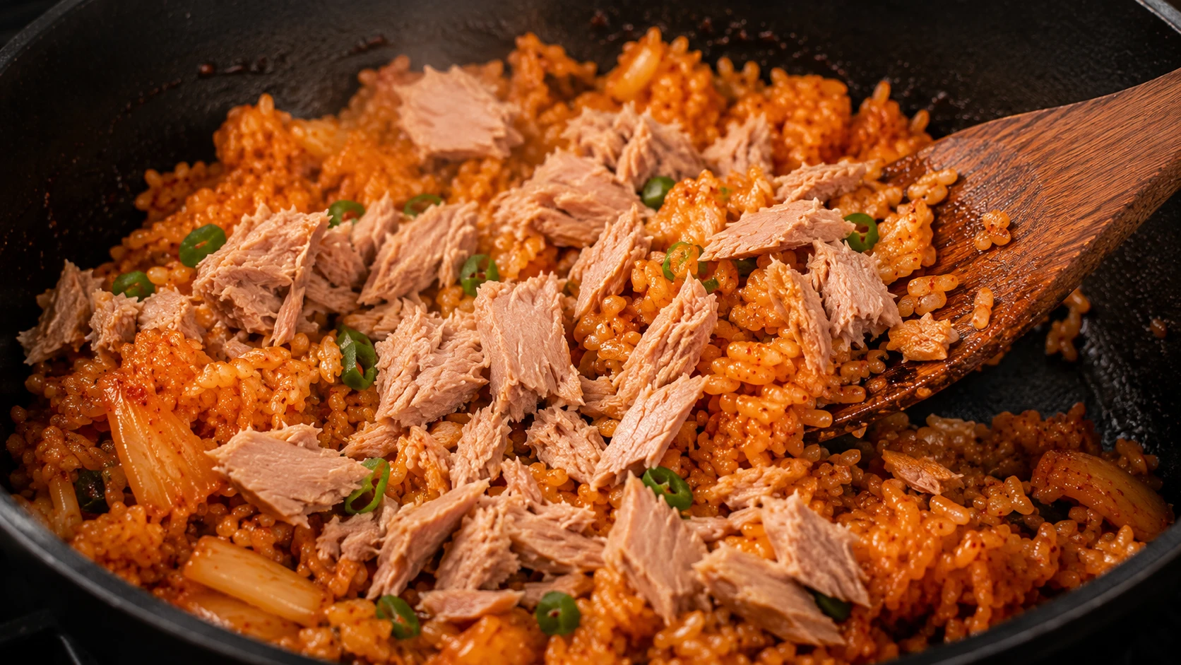 Folding flaked tuna gently into seasoned kimchi rice off heat